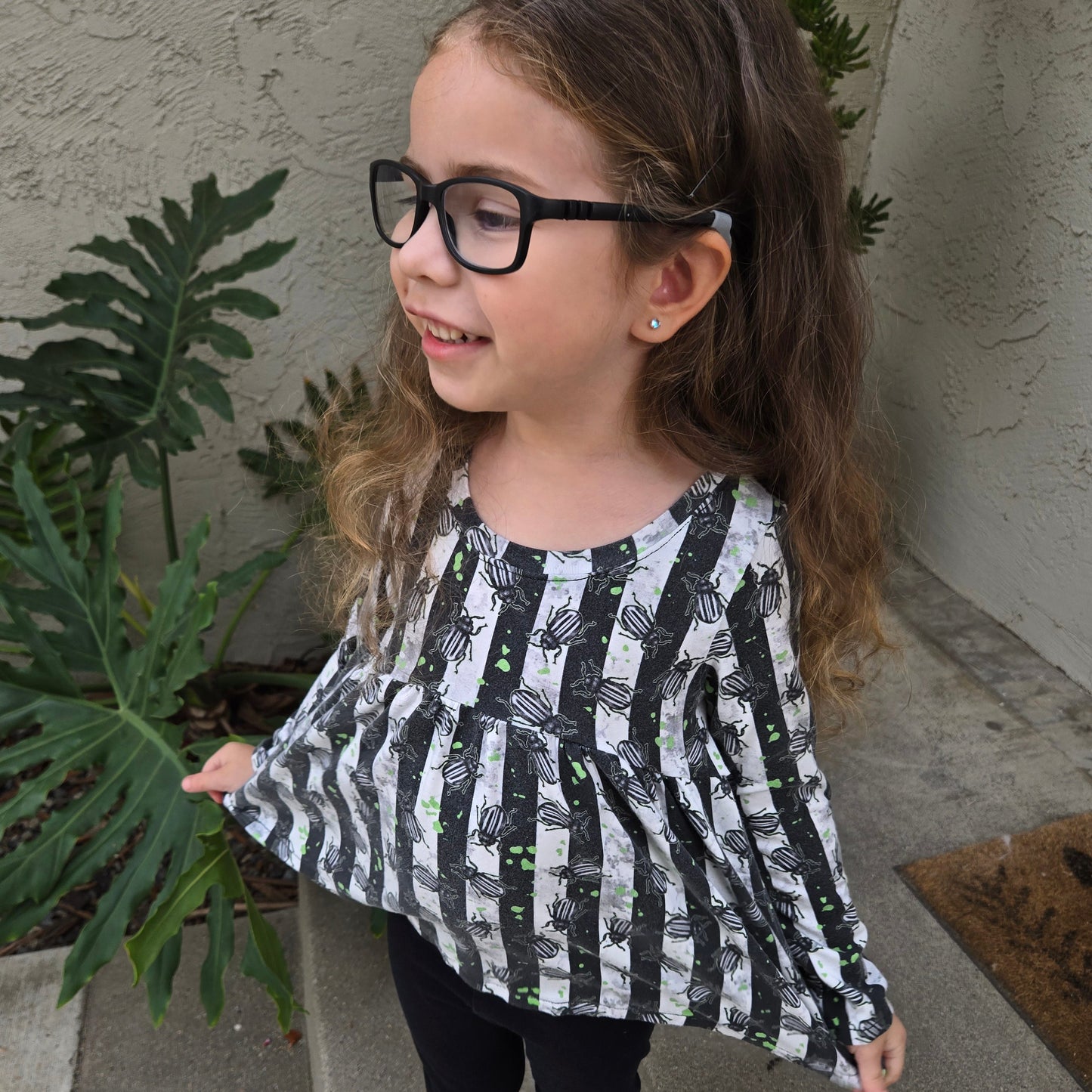 Girl wearing a goth peplum top, with black and white stripes and bugs on it.