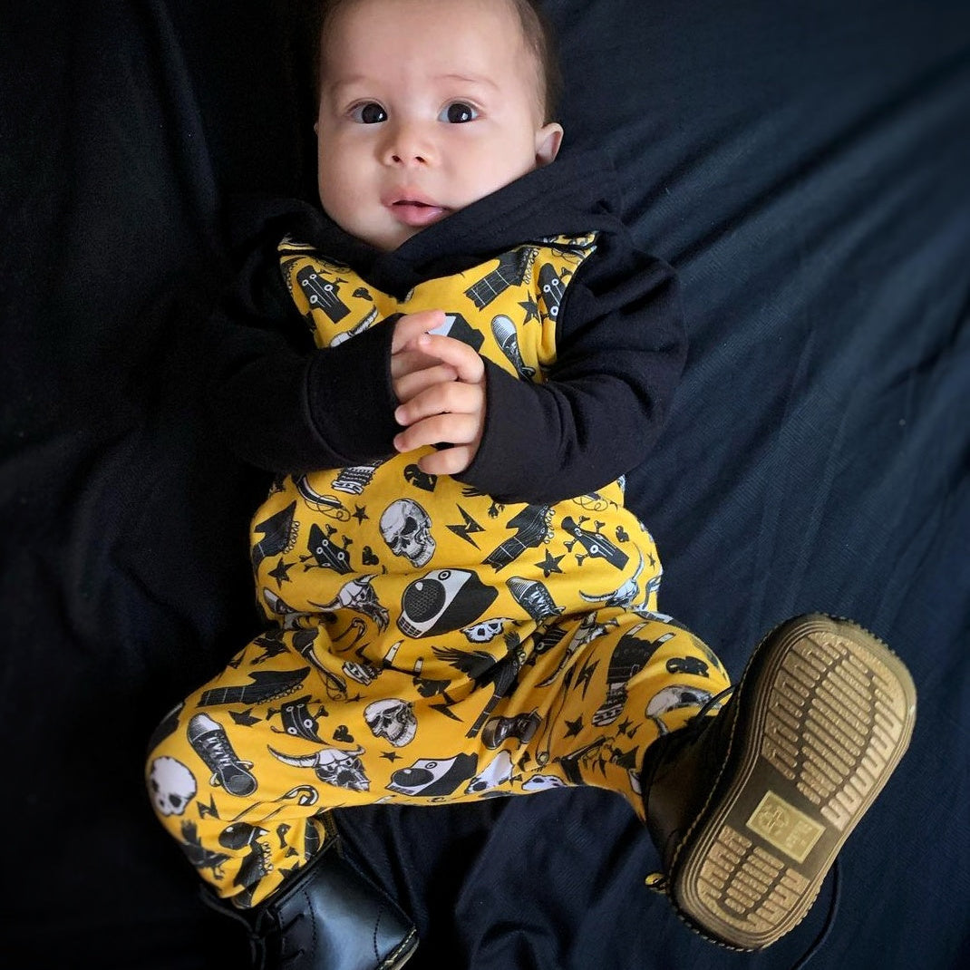 Metal - rock baby wearing a handmade romper with a rock n roll print on it. Yellow, black, white. With Boots.