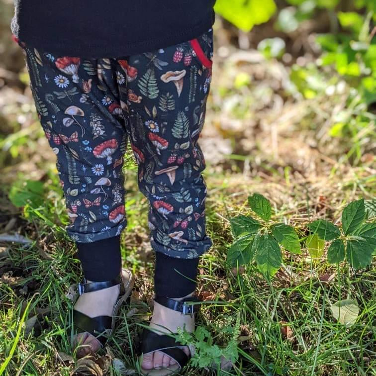 Child wearing dark pants with a nature-themed pattern standing in grass.