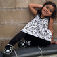 Child wearing alternative clothes : a black and white patterned peplum tank top and shoes with skulls sitting on a ledge against a stone wall.