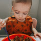 Baby girl wearing a handmade orange spiderweb feeding bib, eating cereals. 