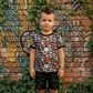 Child wearing a skull-patterned shirt in front of a graffiti-covered wall.