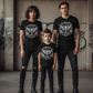 Family of three wearing matching black t-shirts with a white graphic design in an urban setting.