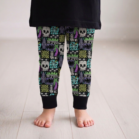 Child wearing colorful skull patterned leggings on a light wooden floor.