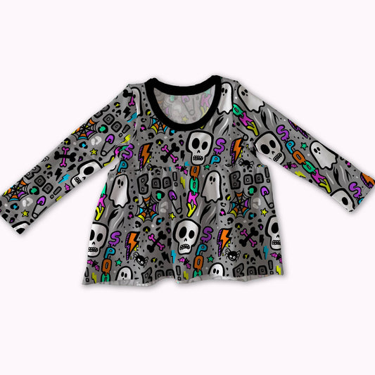 A long-sleeve baby/toddler top with a gray base covered in a colorful Halloween pattern of skulls, ghosts, lightning bolts, and tombstones, featuring a black crew neck.