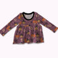 A long-sleeve baby dress in a dusty purple color, decorated with a Halloween pattern of orange pumpkins, black witch hats, and white flowers. It features a black ribbed crew neck and is displayed against a plain white background.