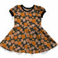 A short-sleeve baby dress with a black and orange pumpkin print, featuring a black crew neck and black sleeve cuffs, shown on a white background.