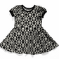 Goth baby or toddler dress,  short sleeves, black and white checkered with contrasting skulls on each square.  Black bands on neck and sleeves. 