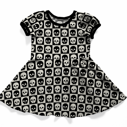 Goth baby or toddler dress,  short sleeves, black and white checkered with contrasting skulls on each square.  Black bands on neck and sleeves. 