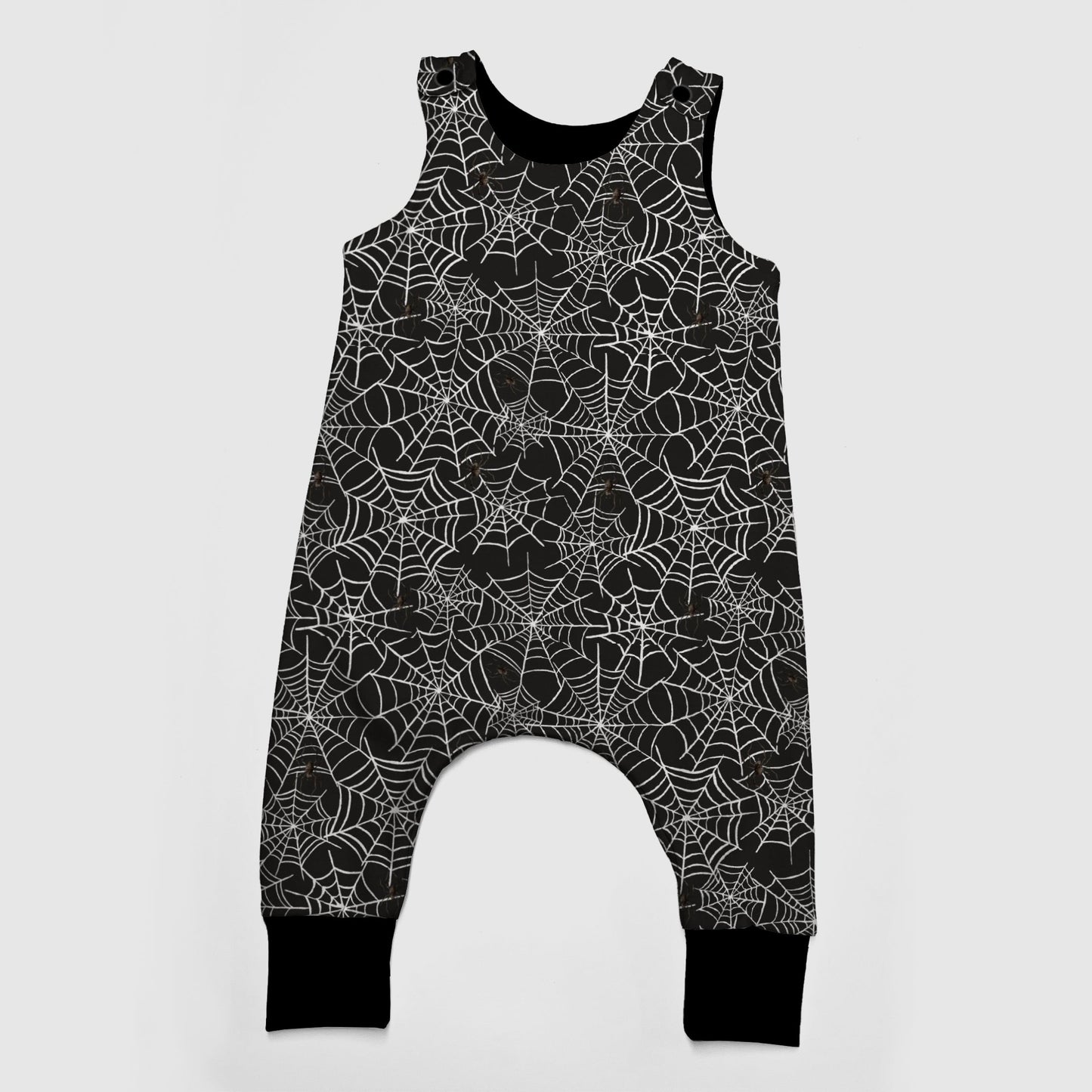 A sleeveless baby romper with an all-over white spiderweb pattern on a black background, featuring a snap-button crotch and black ribbed ankle cuffs, shown against a light gray background.