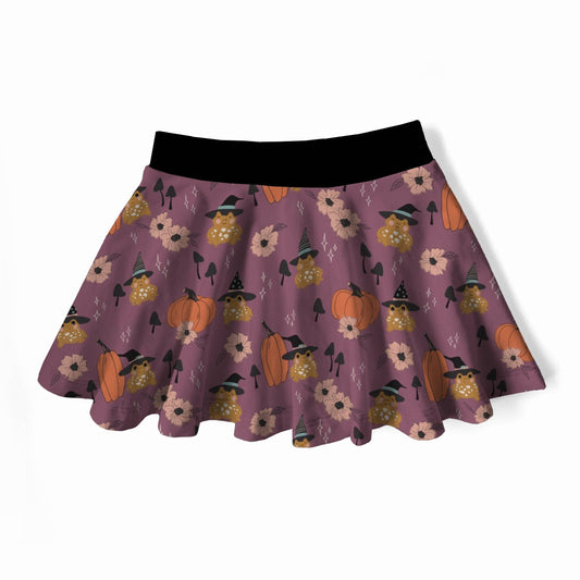 A girls flared skirt with a purple base featuring a Halloween pattern of pumpkins, witch hats, and flowers, finished with a solid black waistband.